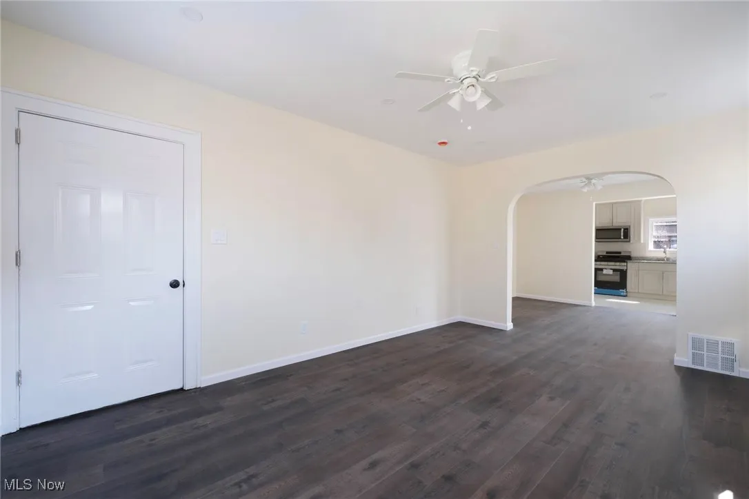 Spare room with a ceiling fan, visible vents, baseboards, arched walkways, and dark wood-type flooring