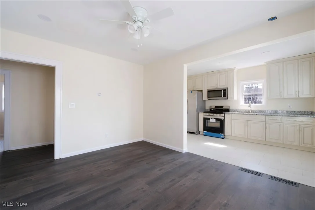 Kitchen with cream cabinetry, wood finished floors, appliances with stainless steel finishes, baseboards, and ceiling fan