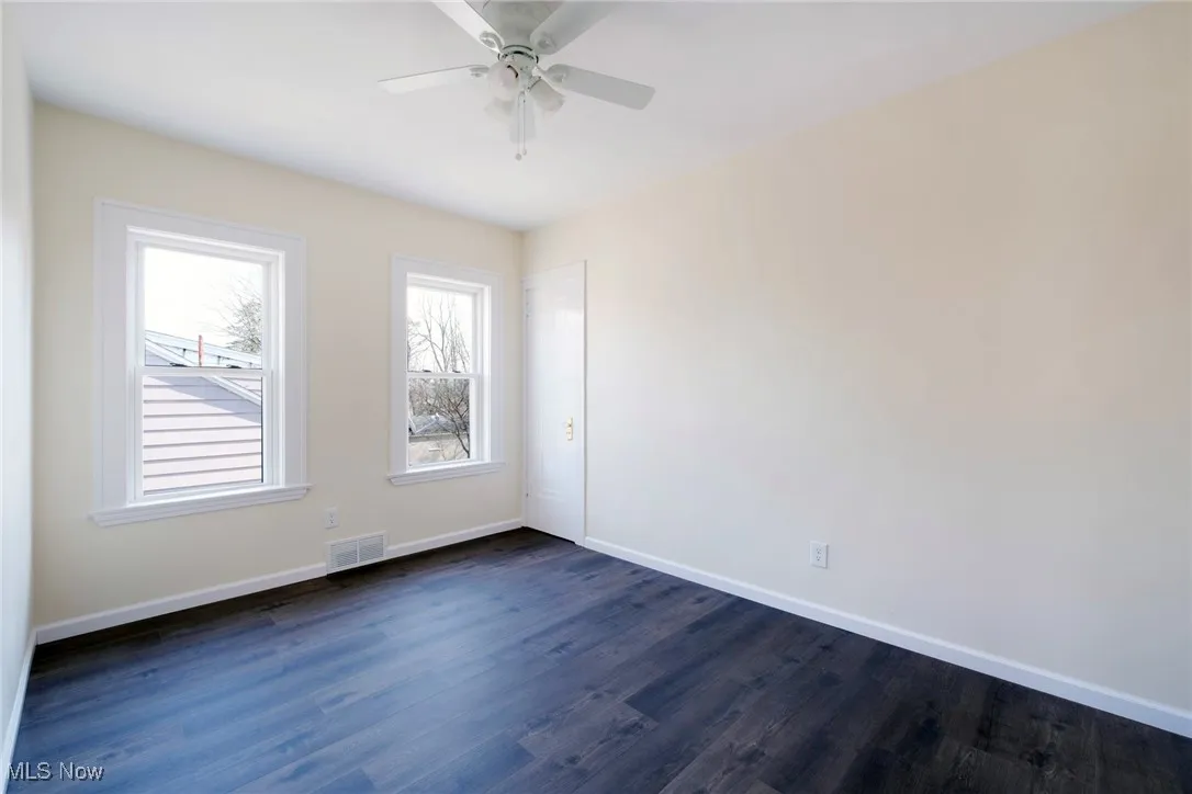 Spare room featuring visible vents, a ceiling fan, dark wood-type flooring, and baseboards