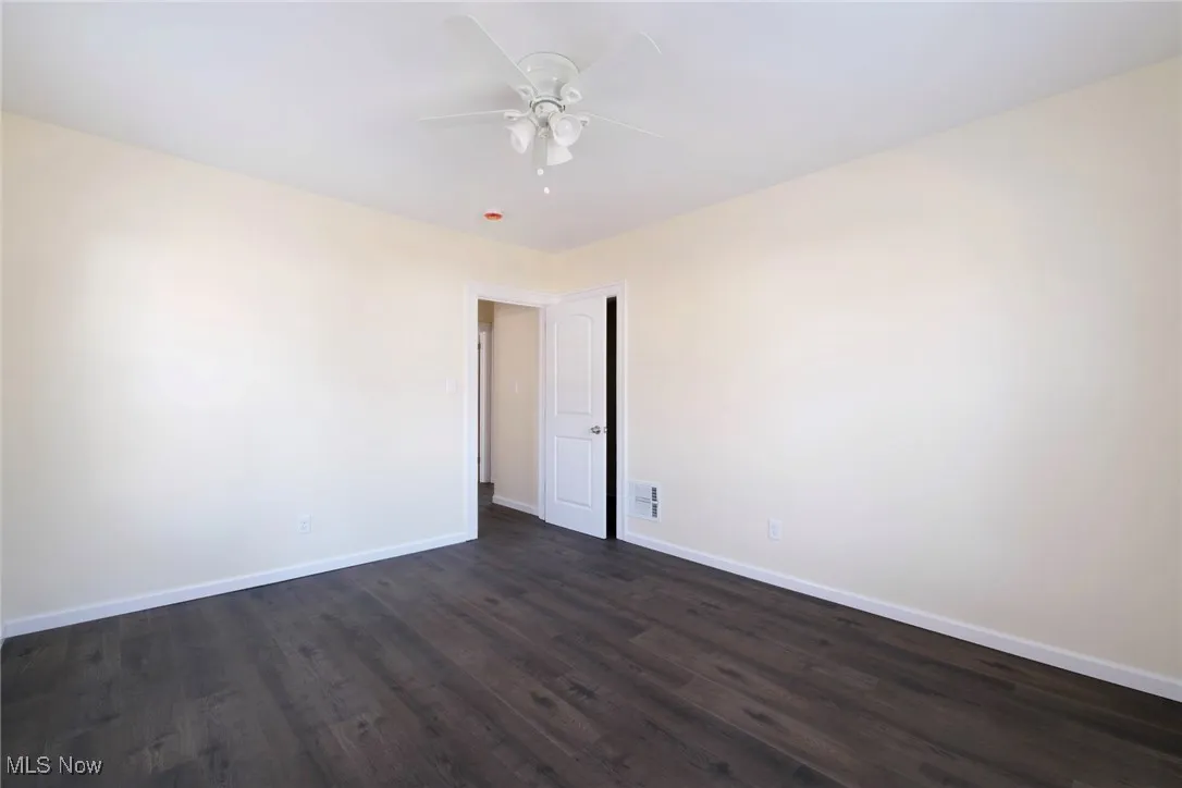 Unfurnished room with dark wood finished floors, visible vents, baseboards, and ceiling fan