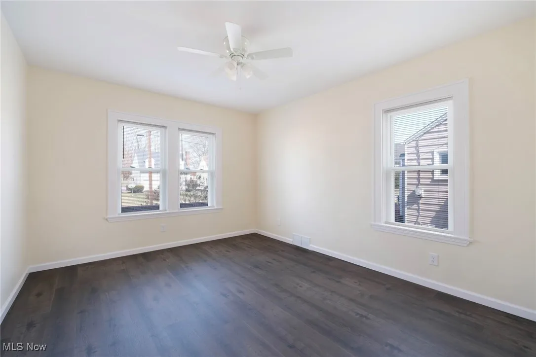 Unfurnished room with ceiling fan, visible vents, baseboards, and dark wood finished floors