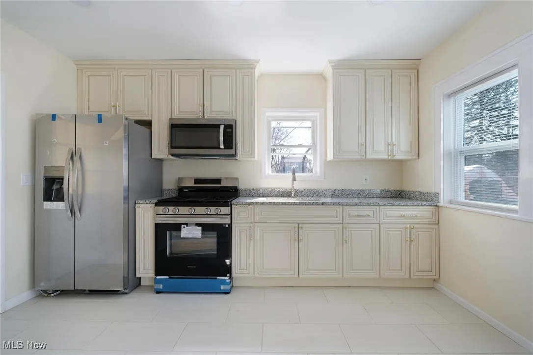 Kitchen featuring a sink, cream cabinets, light stone counters, and stainless steel appliances