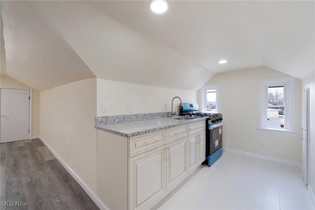 Kitchen featuring gas stove, lofted ceiling, baseboards, and a sink