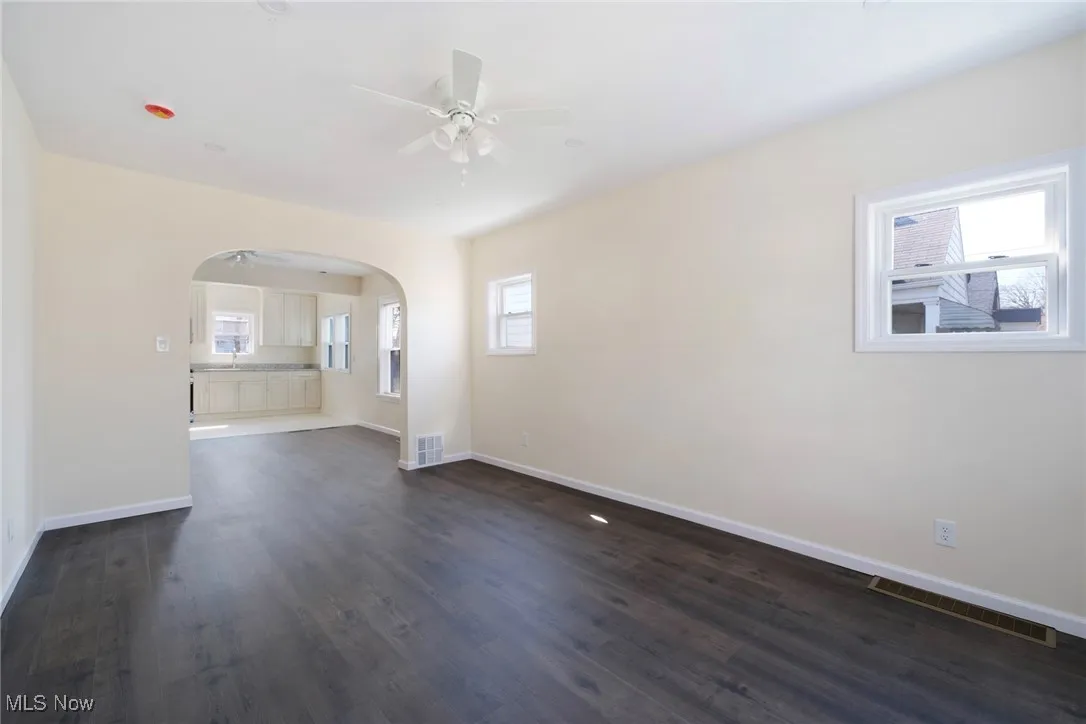 Spare room featuring baseboards, arched walkways, dark wood finished floors, and a ceiling fan