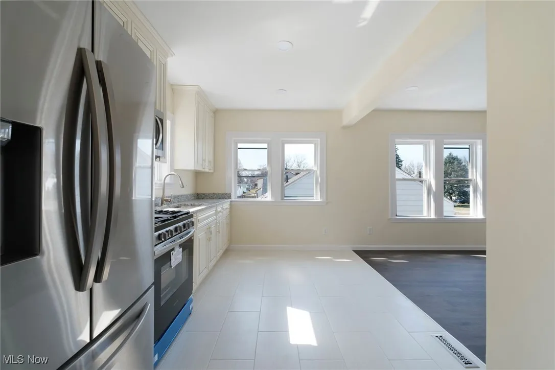 Kitchen featuring baseboards, beamed ceiling, white cabinets, stainless steel appliances, and a sink