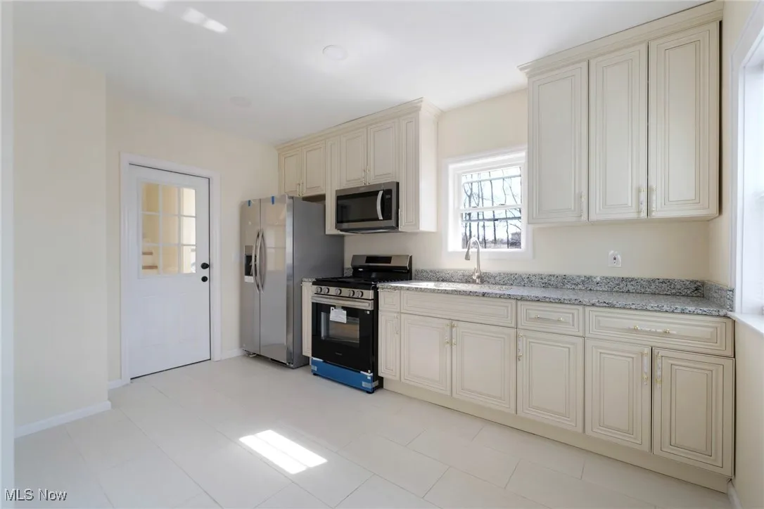 Kitchen with cream cabinets, light stone counters, appliances with stainless steel finishes, and a sink