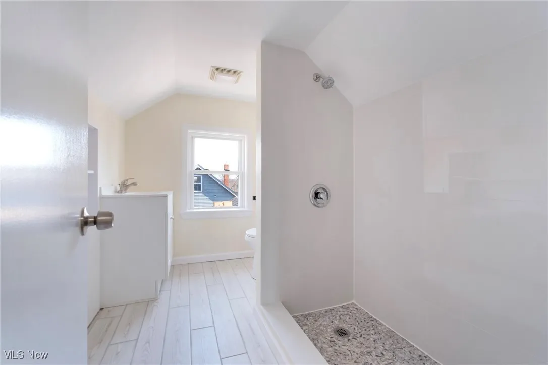 Full bathroom featuring wood finished floors, visible vents, tiled shower, lofted ceiling, and toilet