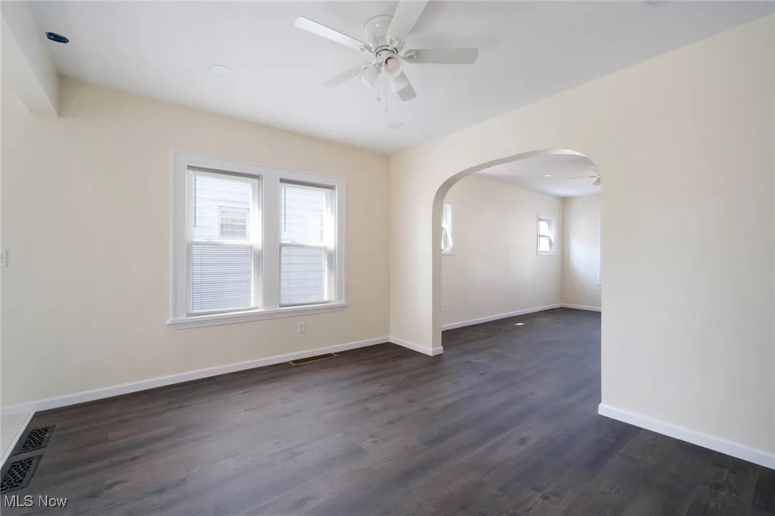 Spare room with visible vents, baseboards, ceiling fan, dark wood-style floors, and arched walkways