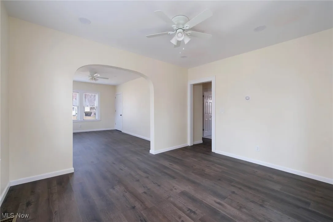 Empty room with baseboards, arched walkways, dark wood-type flooring, and ceiling fan