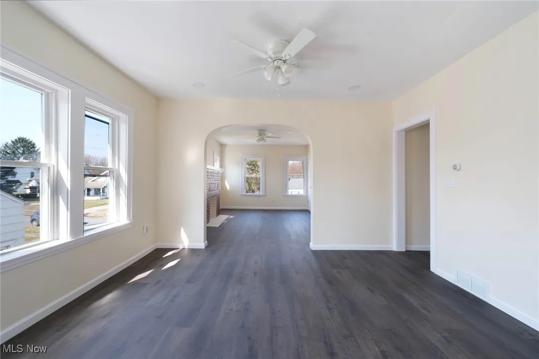 Unfurnished room featuring a ceiling fan, visible vents, baseboards, arched walkways, and dark wood-type flooring
