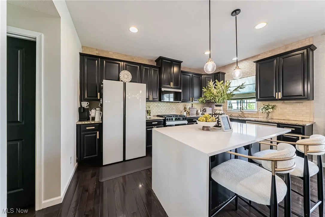 Kitchen featuring a center island, freestanding refrigerator, tasteful backsplash, light countertops, and dark cabinetry
