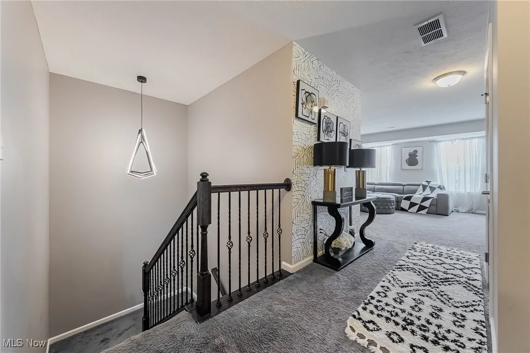Hallway featuring carpet, visible vents, an upstairs landing, and baseboards