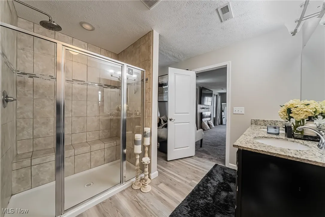 Ensuite bathroom featuring a shower stall, vanity, visible vents, and wood finished floors