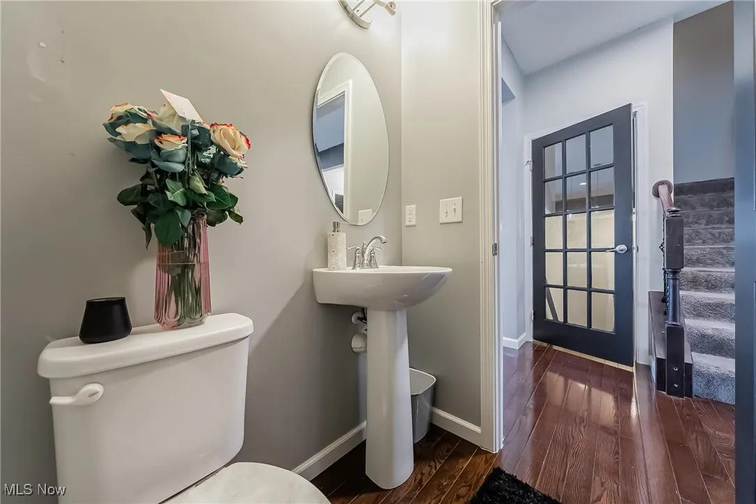 Half bathroom featuring wood finished floors, toilet, and baseboards