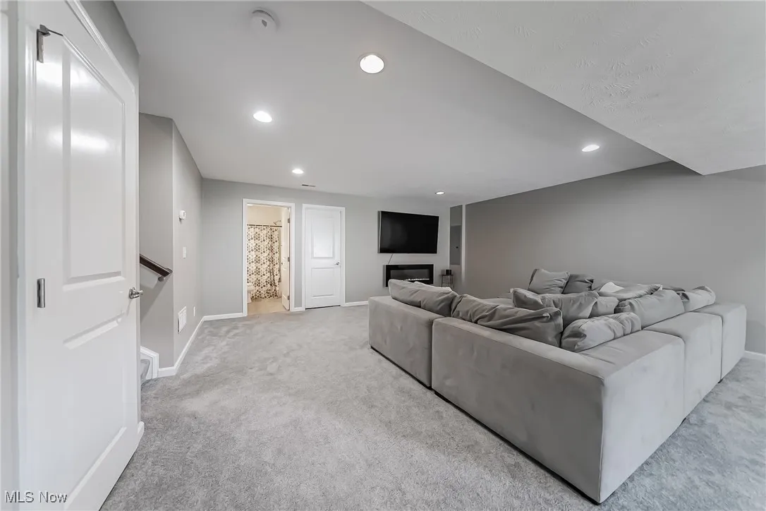 Carpeted living area with baseboards, a glass covered fireplace, and recessed lighting