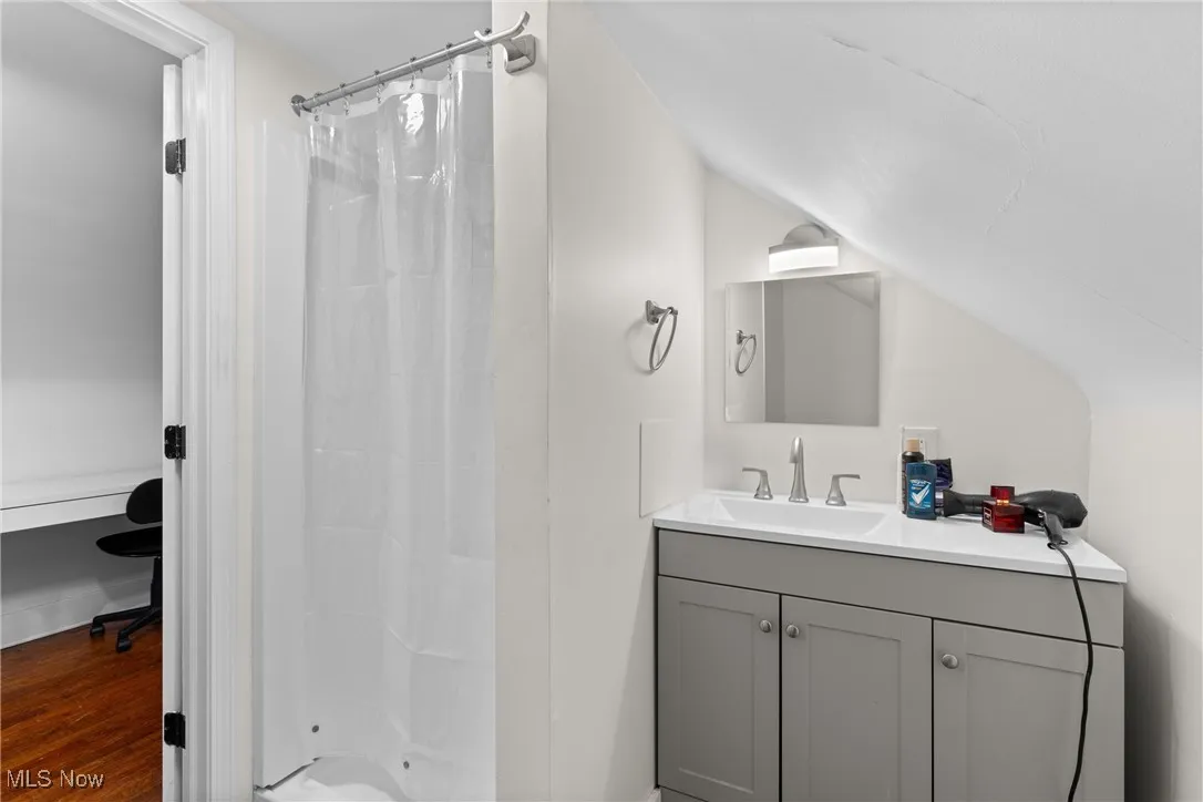 Bathroom with vanity, curtained shower, vaulted ceiling, and wood finished floors