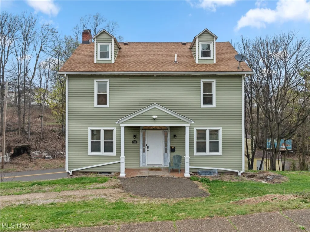 View of front of property featuring a chimney, a front lawn, and roof with shingles