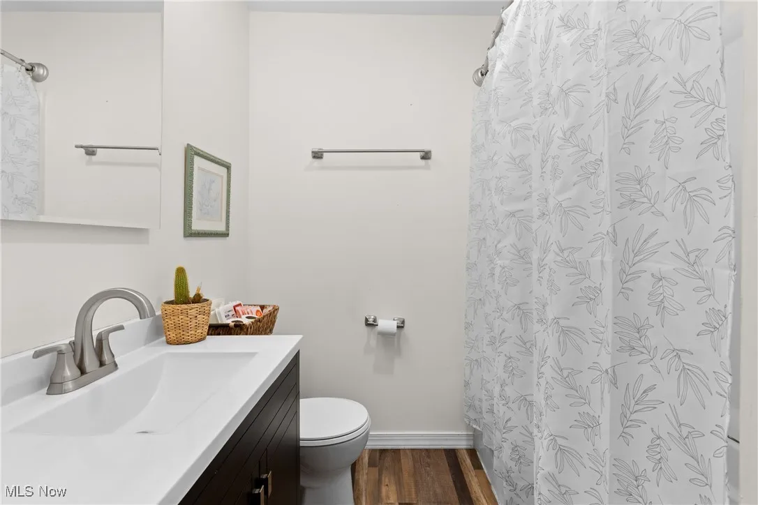 Full bathroom featuring a shower with curtain, vanity, toilet, baseboards, and wood finished floors