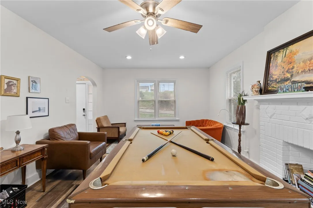 Recreation room featuring recessed lighting, dark wood-type flooring, arched walkways, ceiling fan, and a fireplace