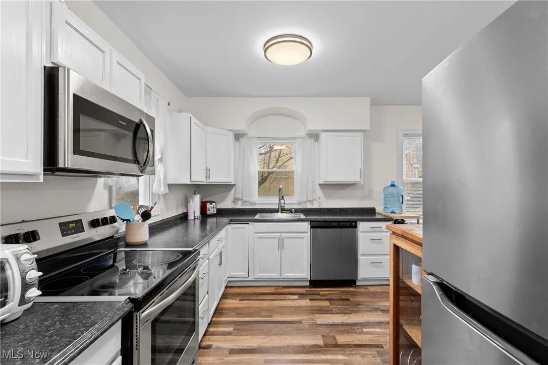 Kitchen with a sink, white cabinets, wood finished floors, and appliances with stainless steel finishes