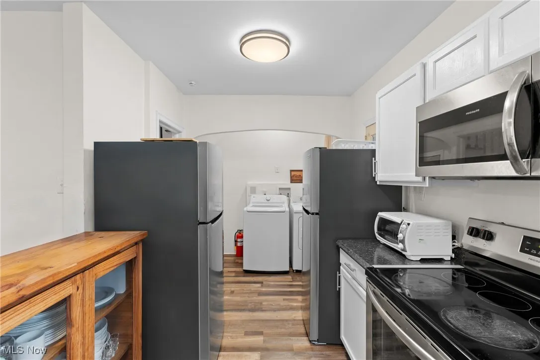 Kitchen featuring light wood-style flooring, stainless steel appliances, a toaster, dark countertops, and white cabinets