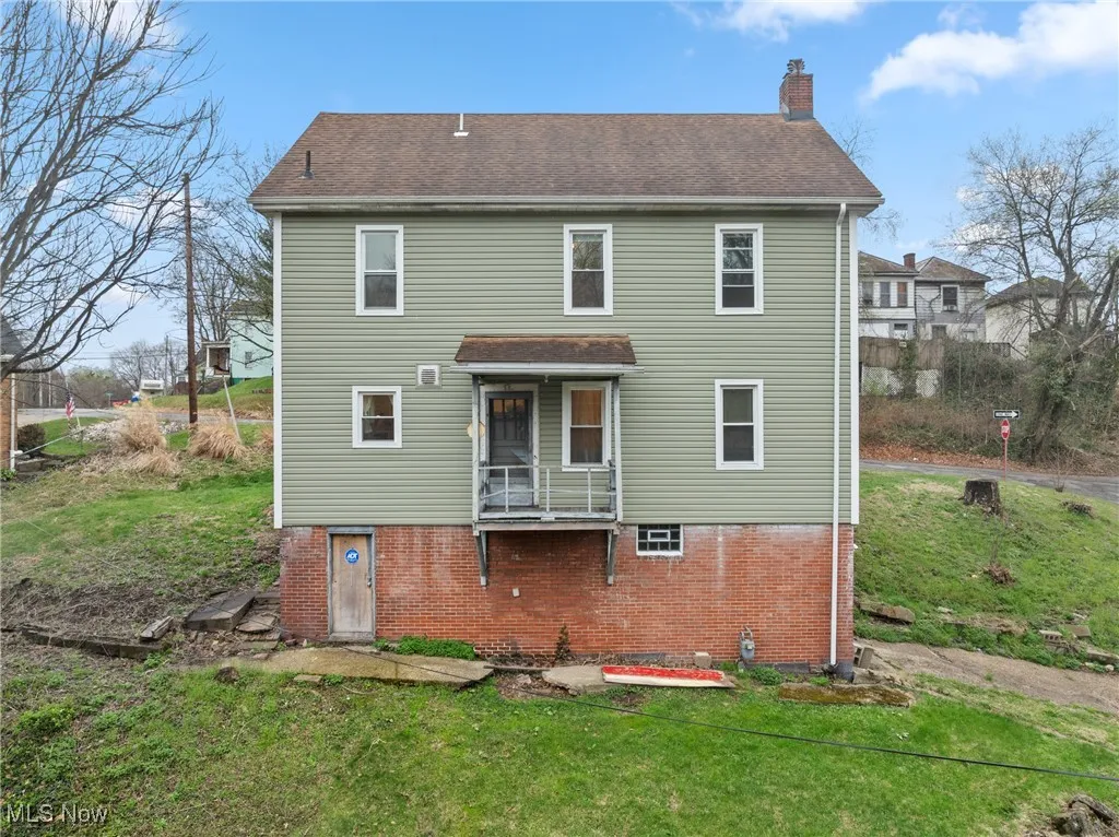 Back of property featuring brick siding, a lawn, roof with shingles, and a chimney
