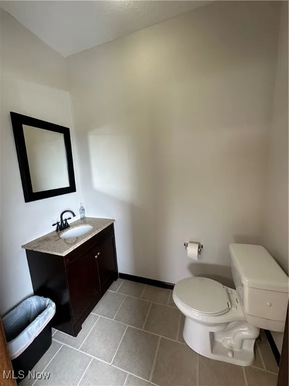 Half bathroom with toilet, vanity, and baseboards