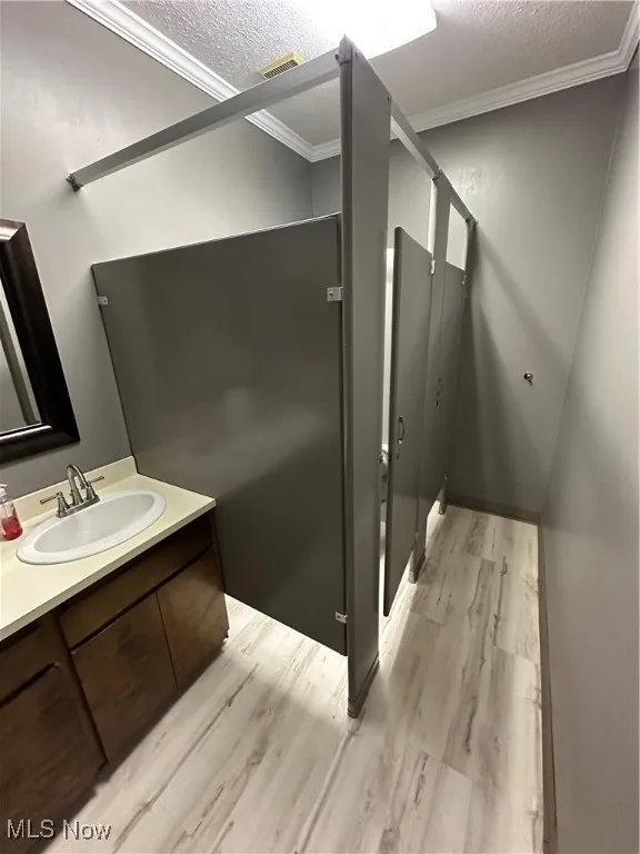Bathroom featuring a textured ceiling, visible vents, ornamental molding, and wood finished floors