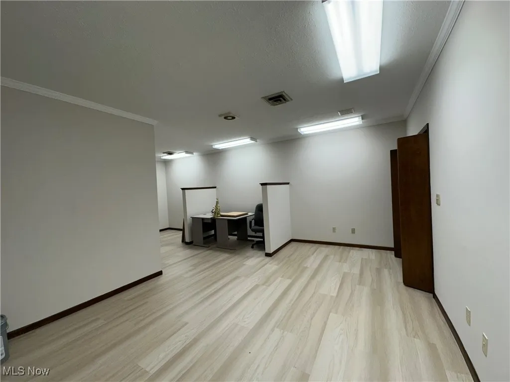 Empty room with baseboards, crown molding, light wood-style floors, and visible vents