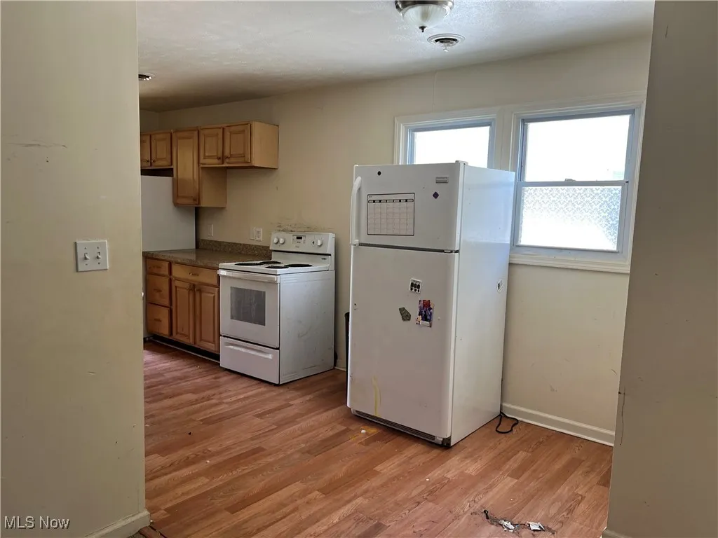 Kitchen with white appliances, light wood-style flooring, dark countertops, baseboards, and light brown cabinetry