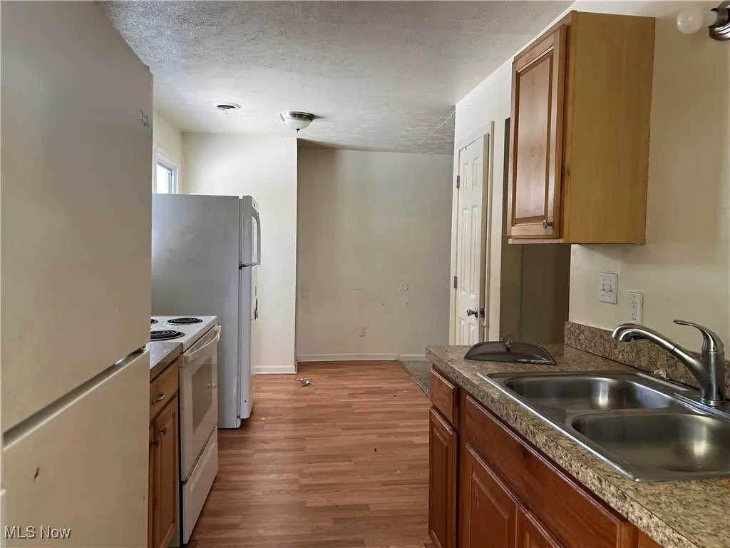 Kitchen with white appliances, a sink, brown cabinets, wood finished floors, and a textured ceiling