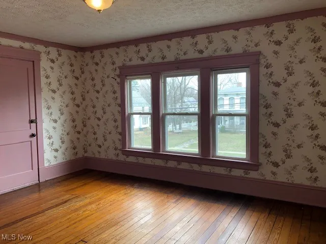 Empty room featuring baseboards, a textured ceiling, light wood-style flooring, and wallpapered walls