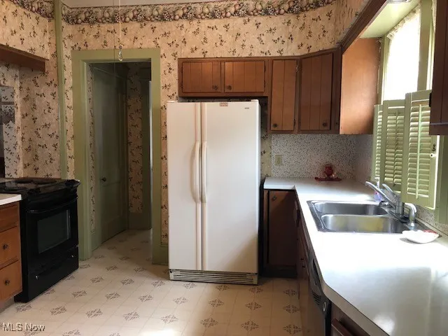Kitchen featuring wallpapered walls, freestanding refrigerator, and a sink