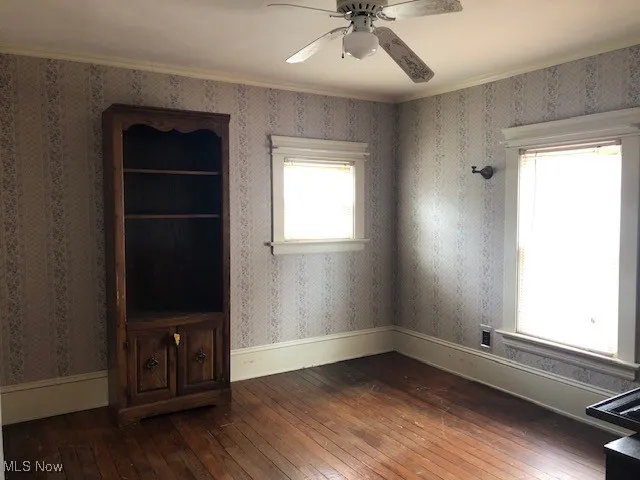 Unfurnished room featuring baseboards, dark wood-type flooring, a ceiling fan, and wallpapered walls