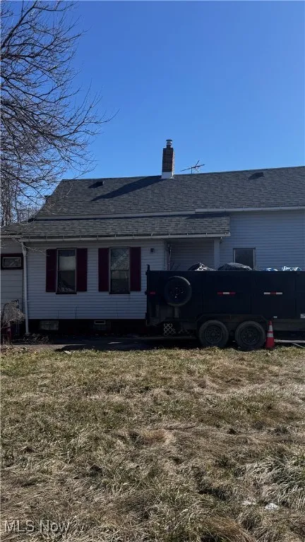 Rear view of property with a lawn, roof with shingles, and a chimney
