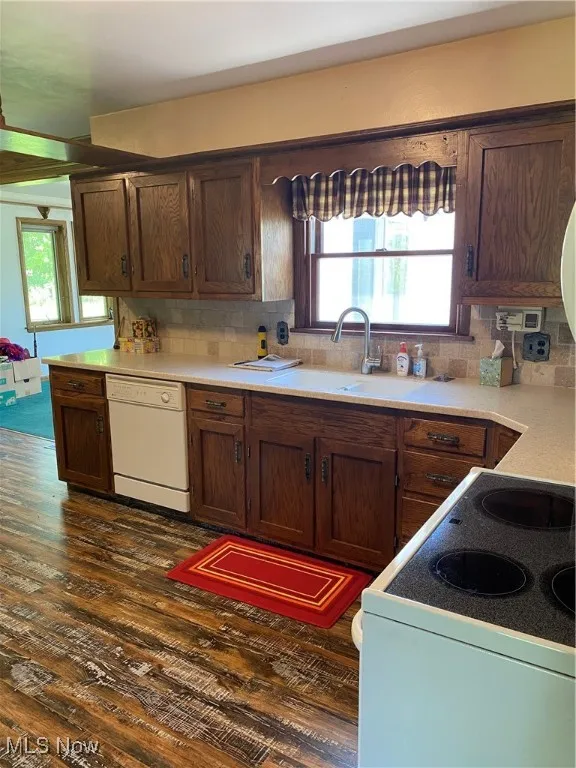 Kitchen with dishwashing machine, stove, a sink, dark wood-style flooring, and decorative backsplash