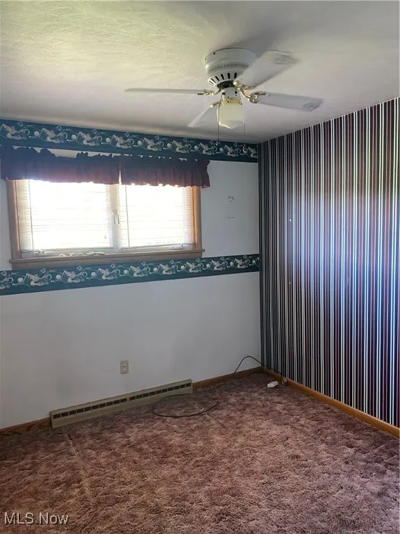 Carpeted empty room with a baseboard heating unit, a ceiling fan, and baseboards