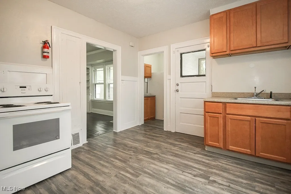 Kitchen featuring a sink, brown cabinetry, dark wood-style floors, and white electric range oven
