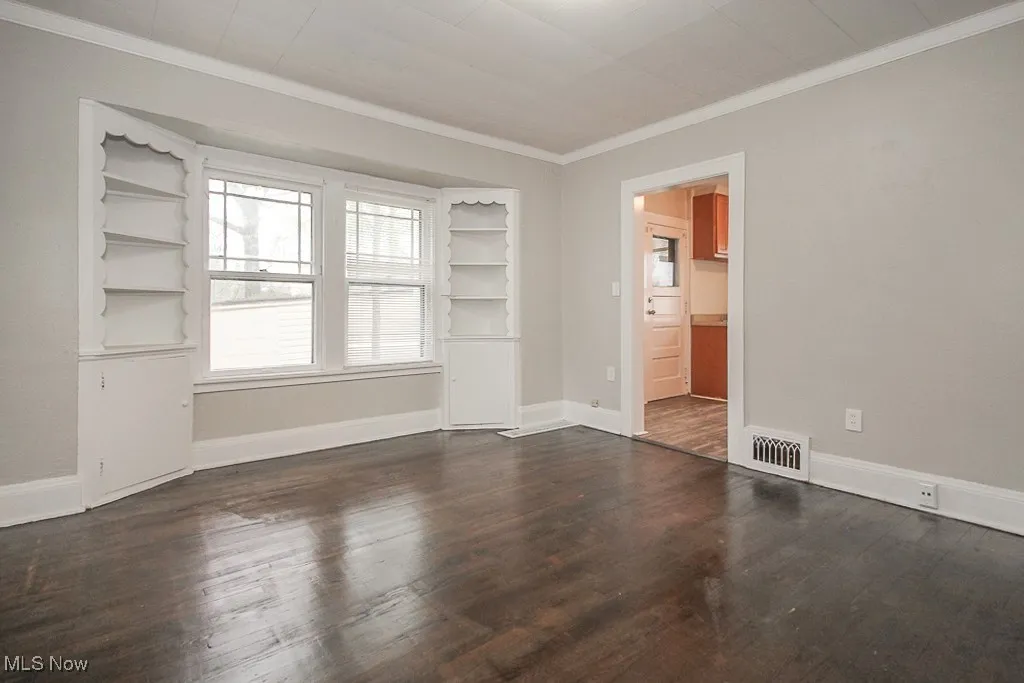 Unfurnished room featuring crown molding, wood finished floors, visible vents, and baseboards