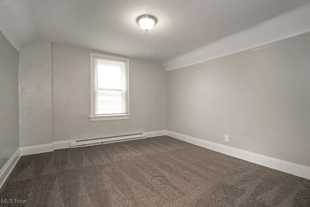 Empty room featuring baseboards, lofted ceiling, baseboard heating, and dark carpet