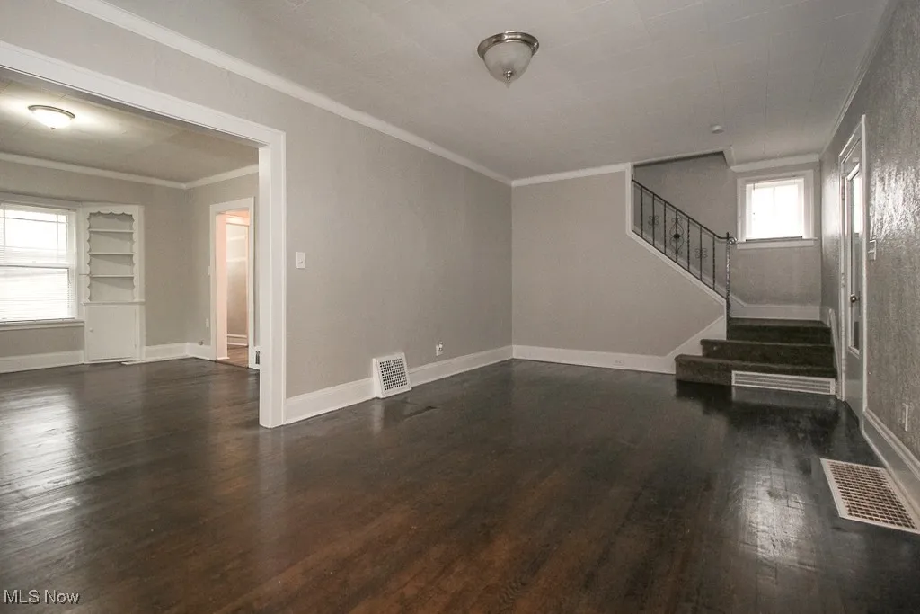 Unfurnished living room featuring visible vents, wood finished floors, ornamental molding, and stairway