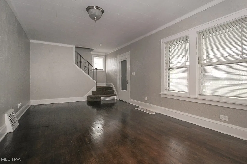 Unfurnished living room featuring crown molding, stairway, wood finished floors, and baseboards