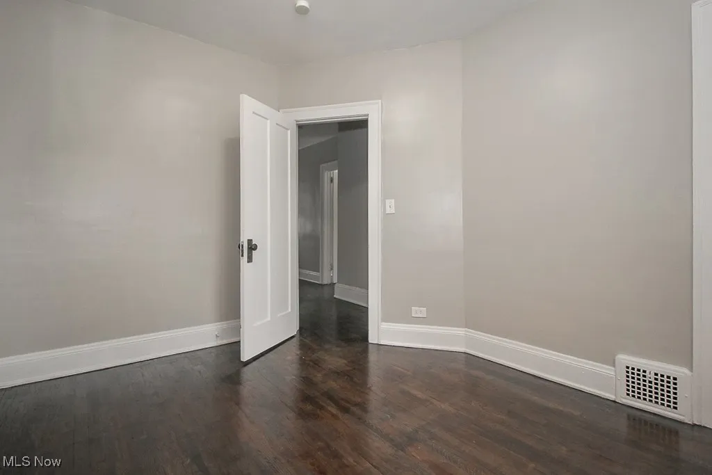 Empty room with visible vents, dark wood-type flooring, and baseboards