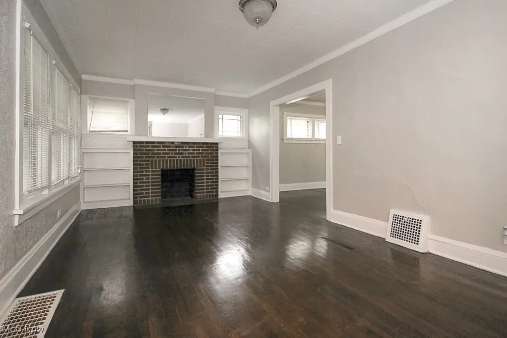 Unfurnished living room featuring dark wood-style floors, visible vents, and a fireplace