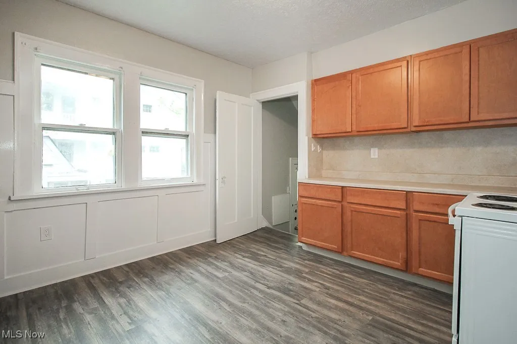 Kitchen with dark wood finished floors, light countertops, electric stove, brown cabinetry, and a decorative wall
