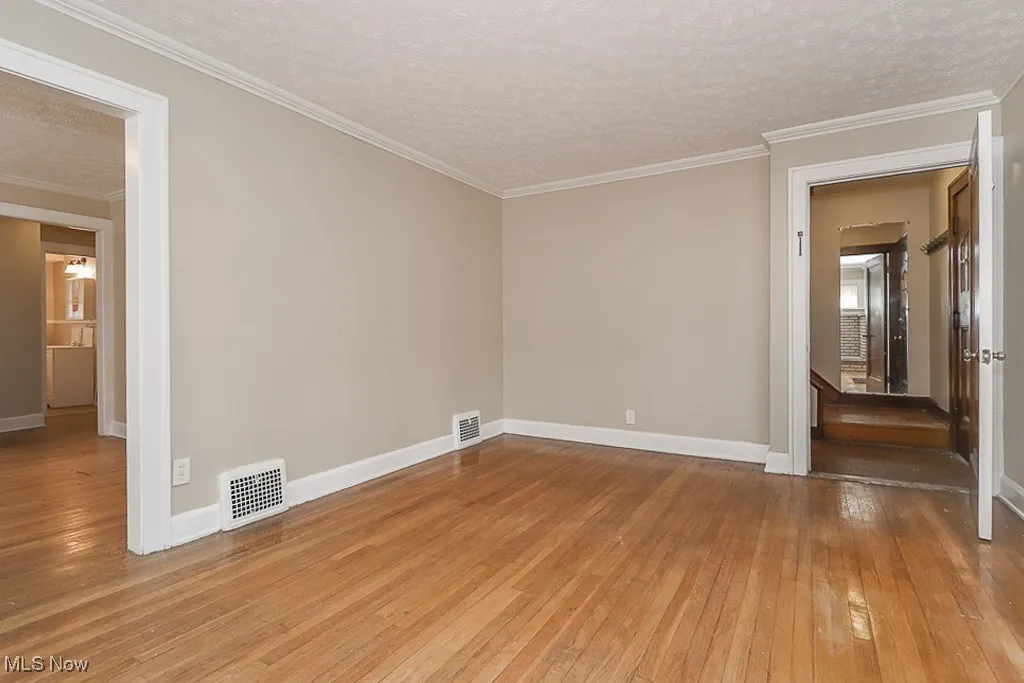 Empty room with visible vents, light wood-style flooring, a textured ceiling, and crown molding