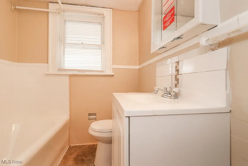 Bathroom featuring vanity, wainscoting, tile walls, toilet, and a washtub
