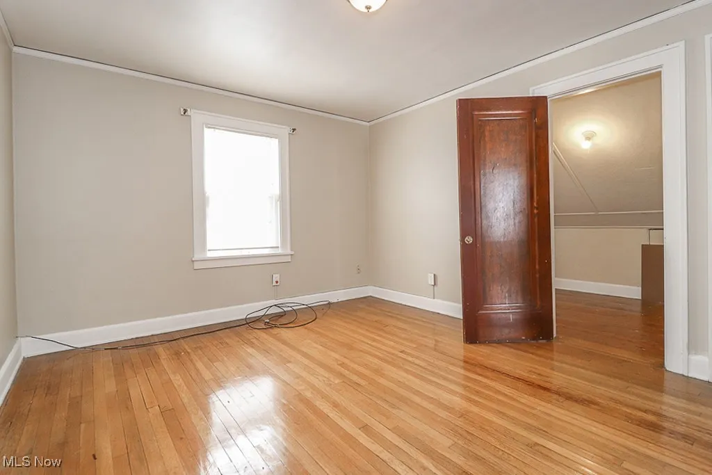 Empty room featuring crown molding, light wood-type flooring, and baseboards