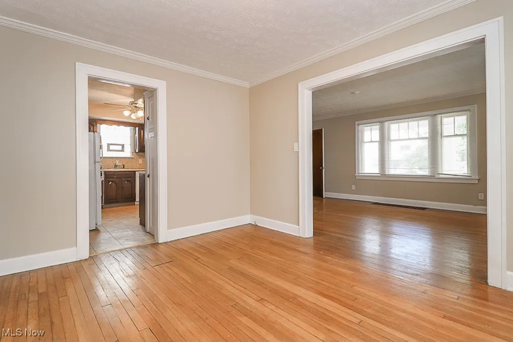 Spare room with ornamental molding, a textured ceiling, light wood-style floors, baseboards, and ceiling fan
