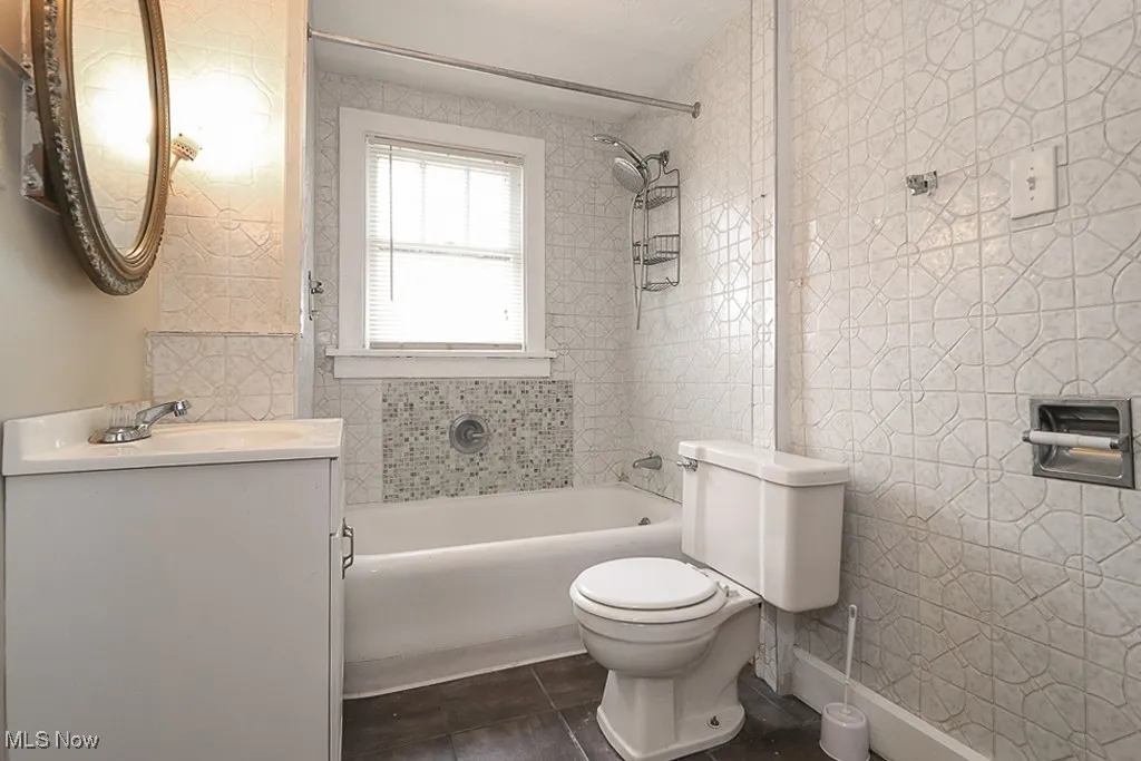 Bathroom featuring toilet, vanity, bathtub / shower combination, tile patterned floors, and tile walls